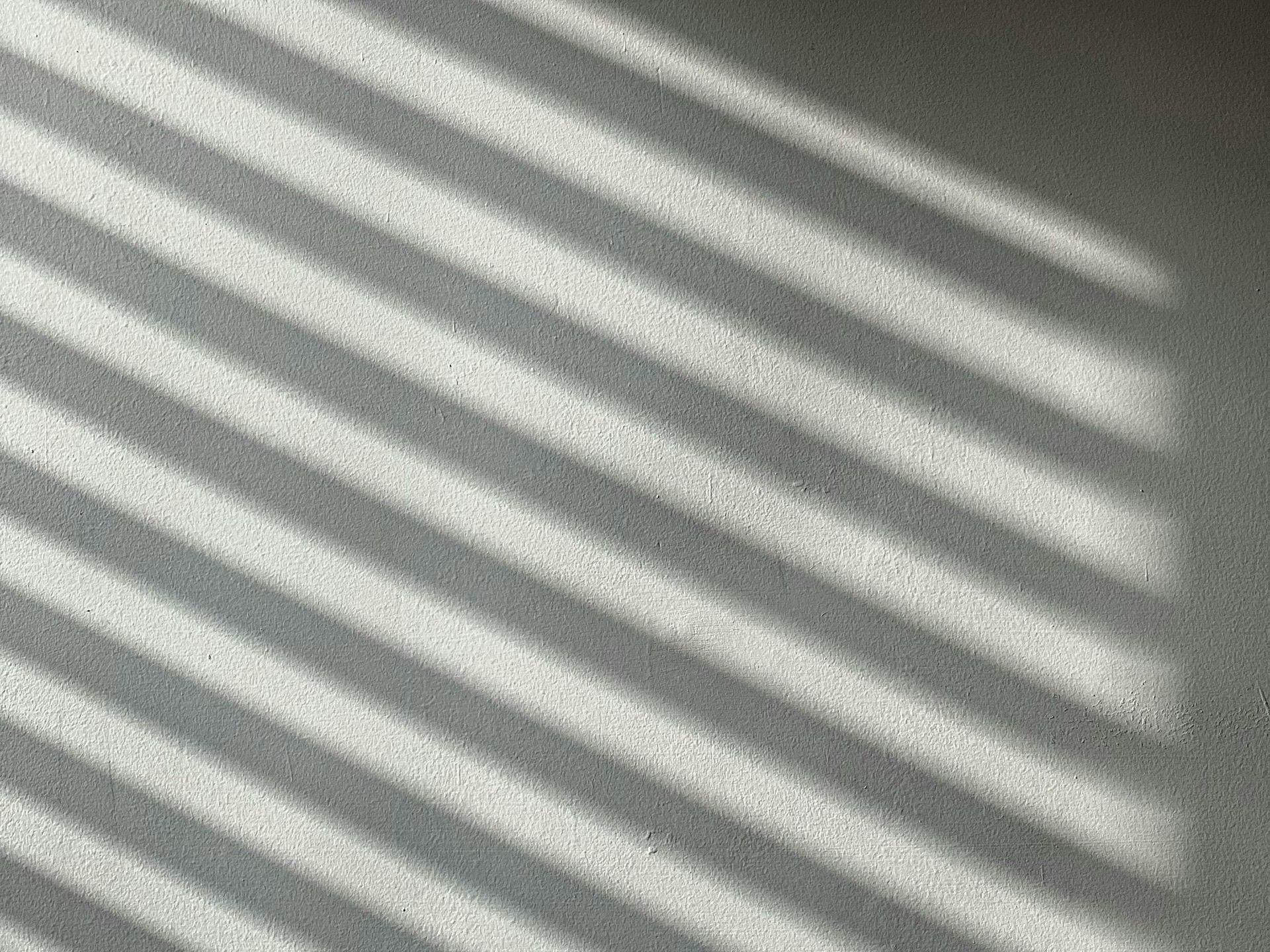 the silhouette of a person leaning against a wall, half hidden by window‑blind shadows, conveying the quiet erosion of awareness and over‑confidence
