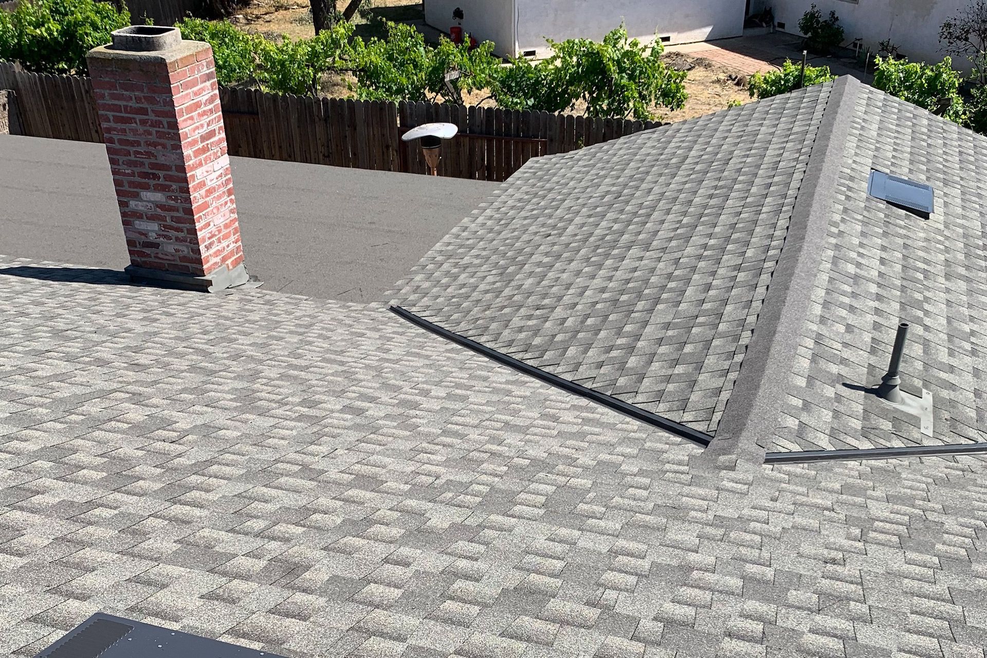 Gray shingle roof with a brick chimney and a small skylight against a sunny backdrop.