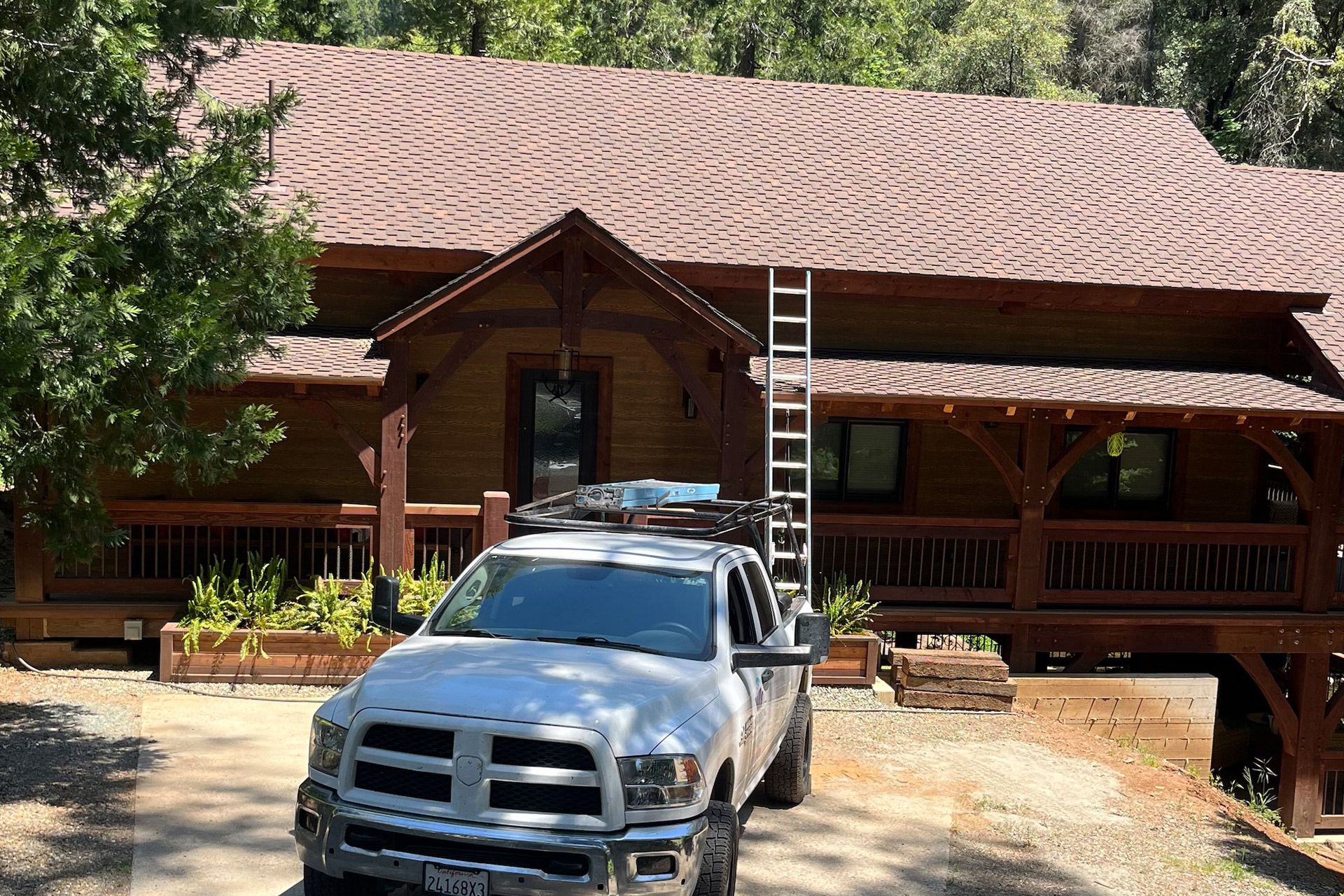 White truck parked in front of a wood cabin-style house; ladder on the roof.