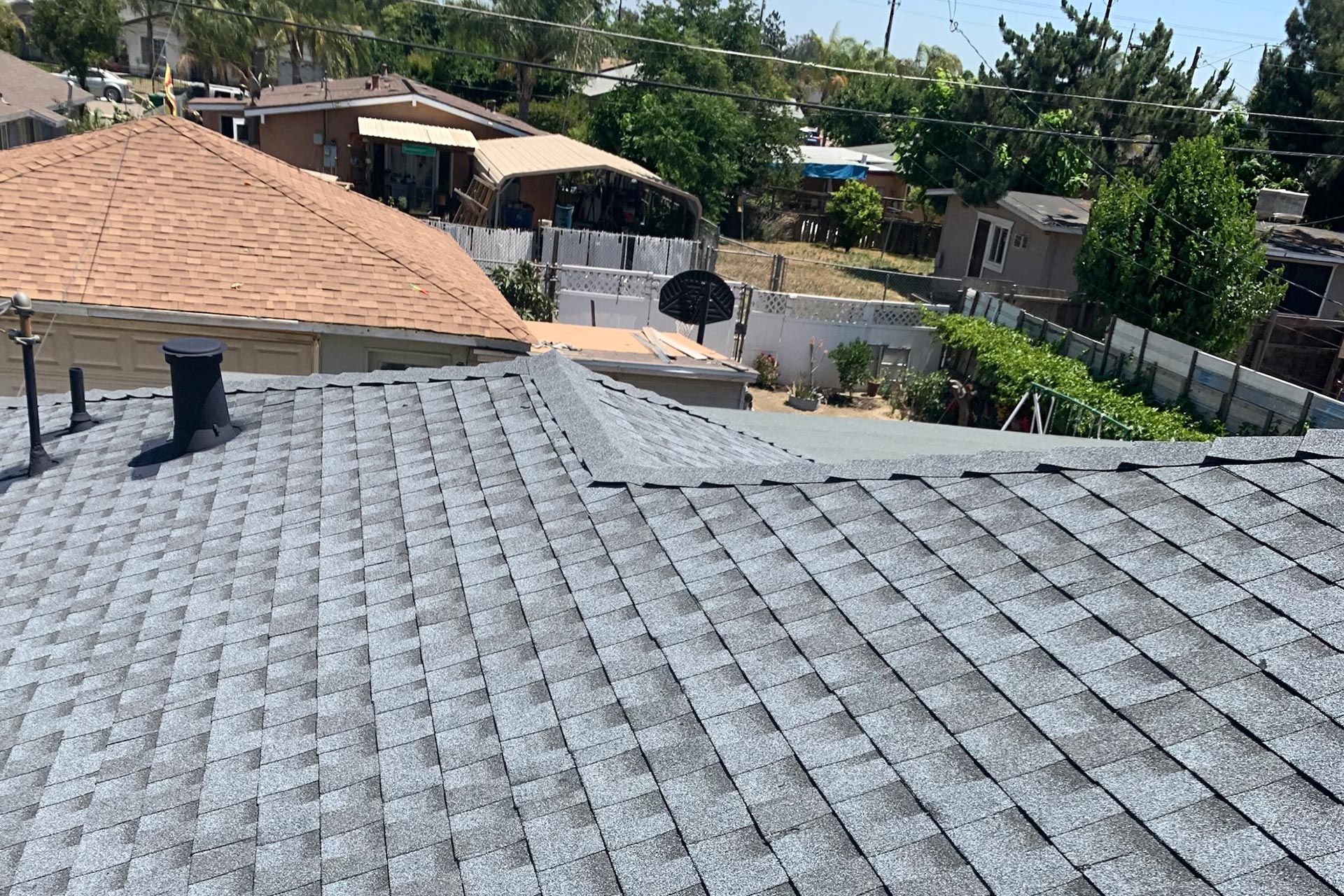 View of rooftops with gray shingles, surrounded by other houses and greenery on a sunny day.