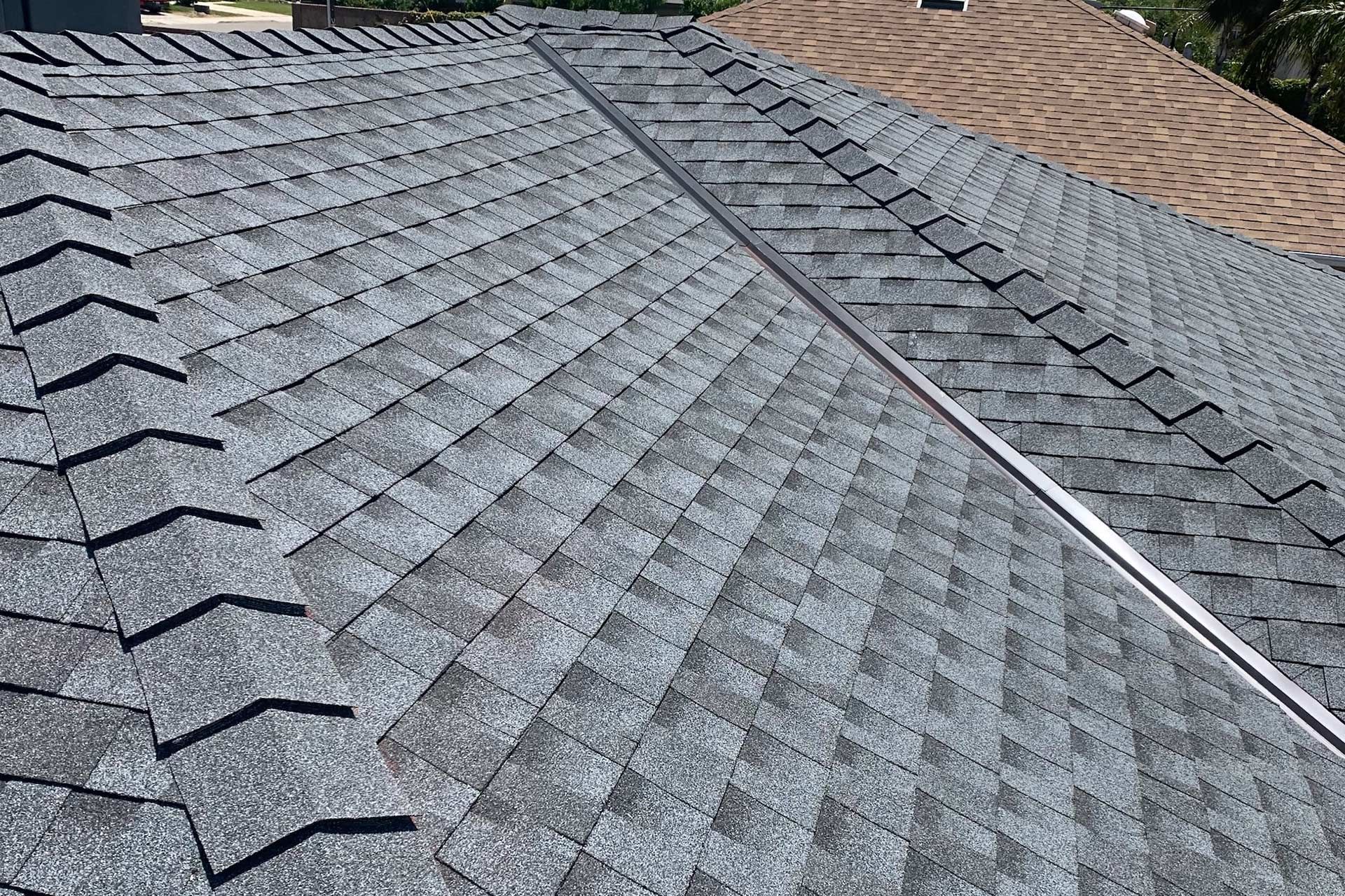 Close-up view of a gray asphalt shingle roof with a central metal ridge flashing.
