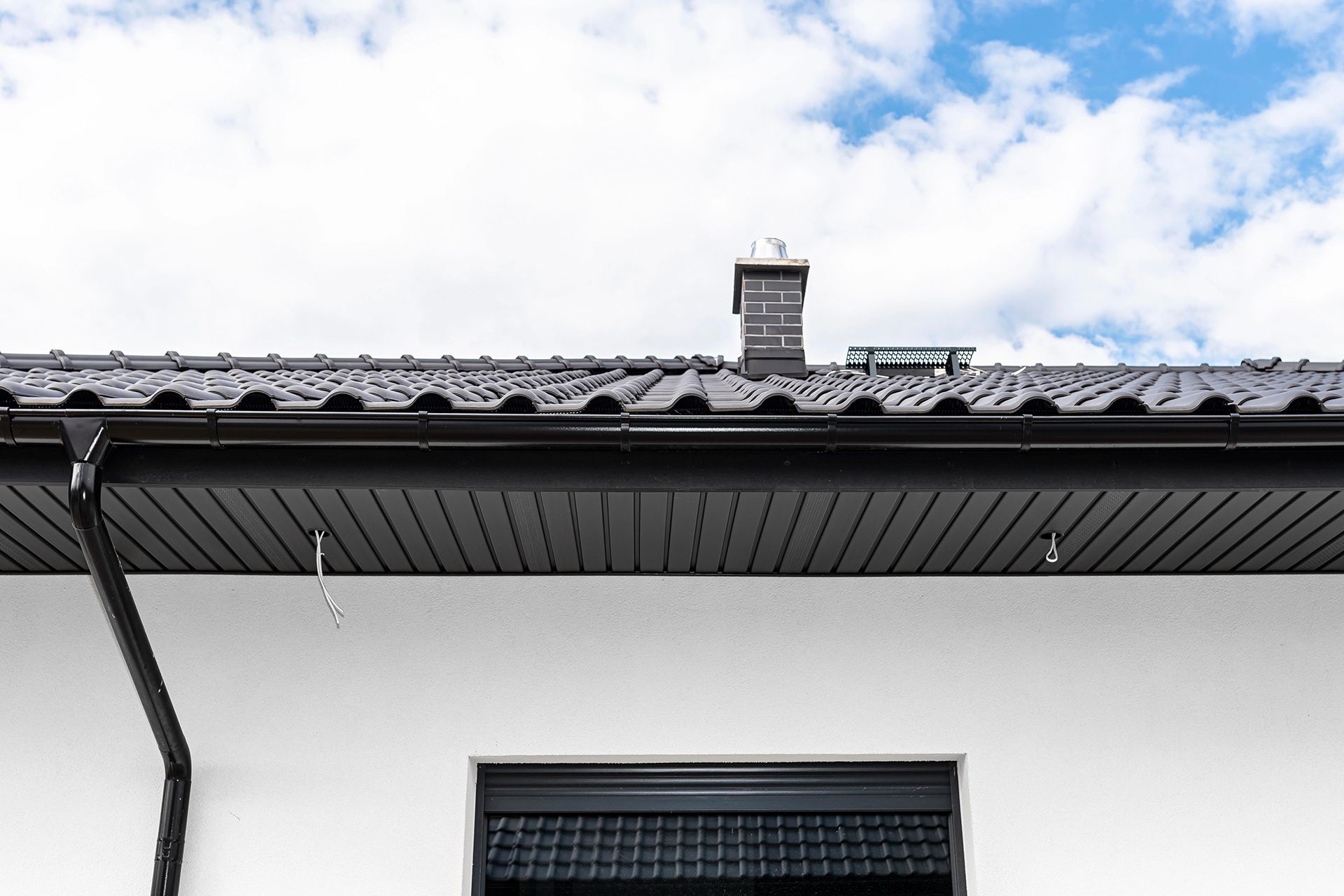 Black roof, gutters, and siding on white house with chimney against blue sky.
