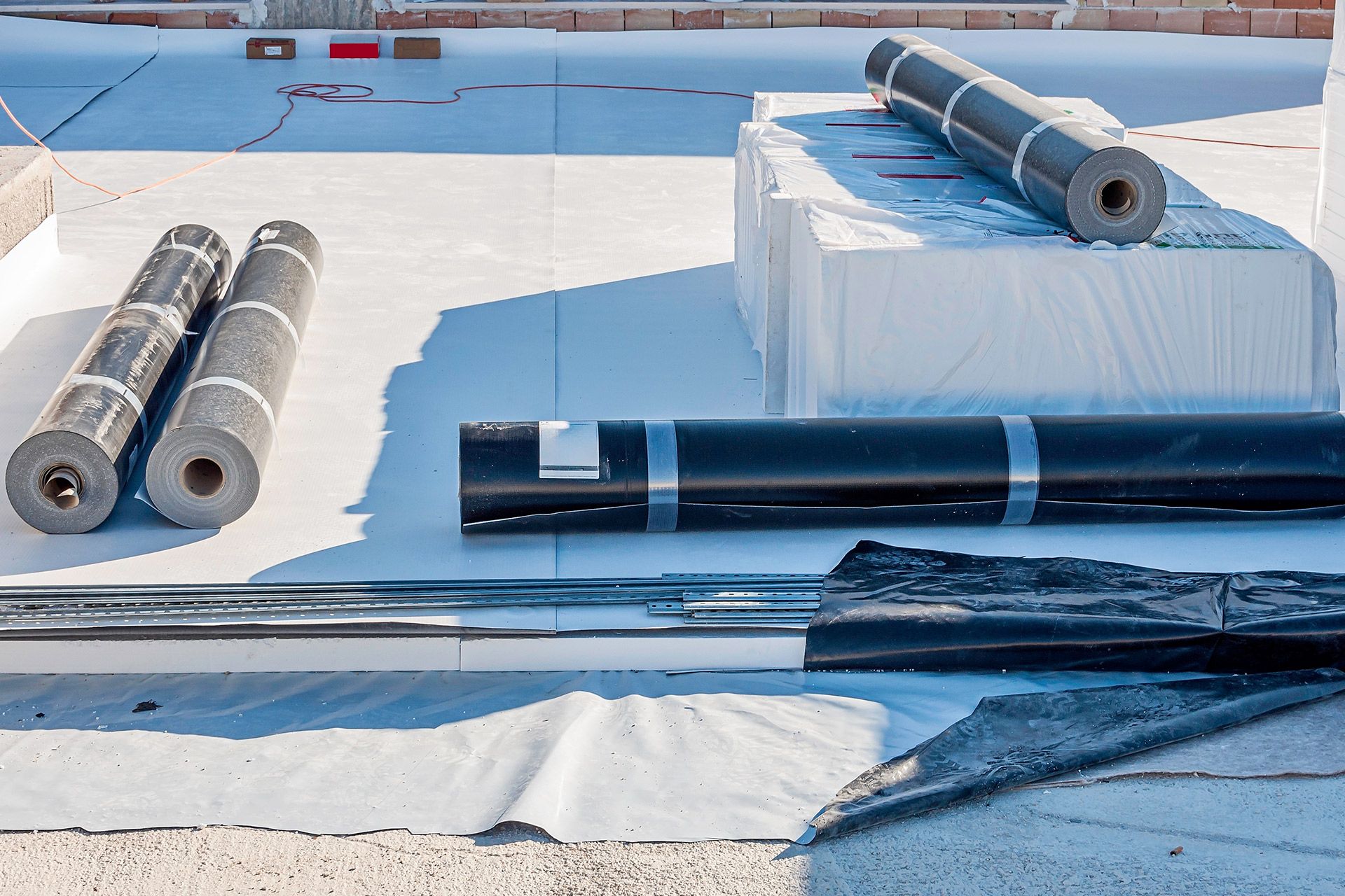 Roofing materials on a flat rooftop. Rolls of black roofing material, insulation, and tools.