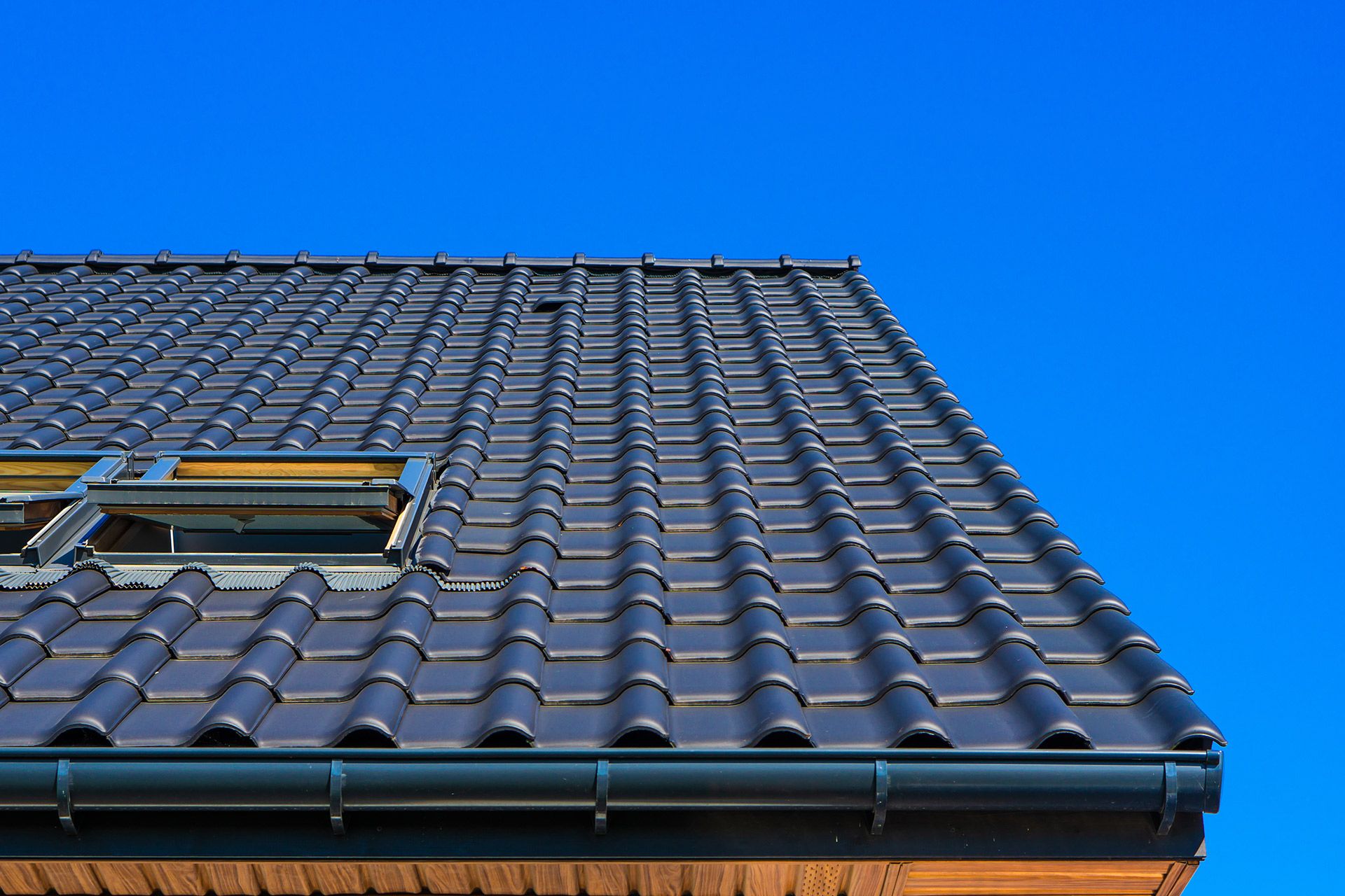 Dark gray tiled roof with black gutter against a clear blue sky.