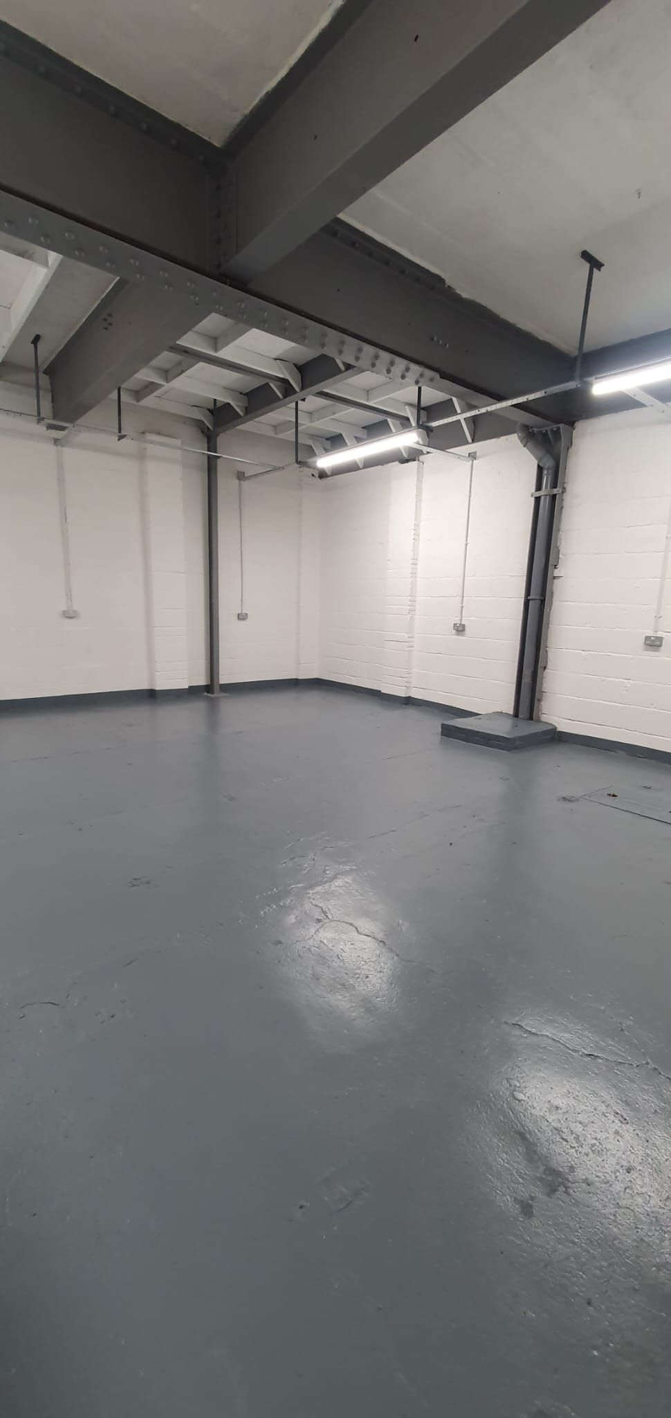 Empty industrial room with white walls, exposed beams, and a gray floor