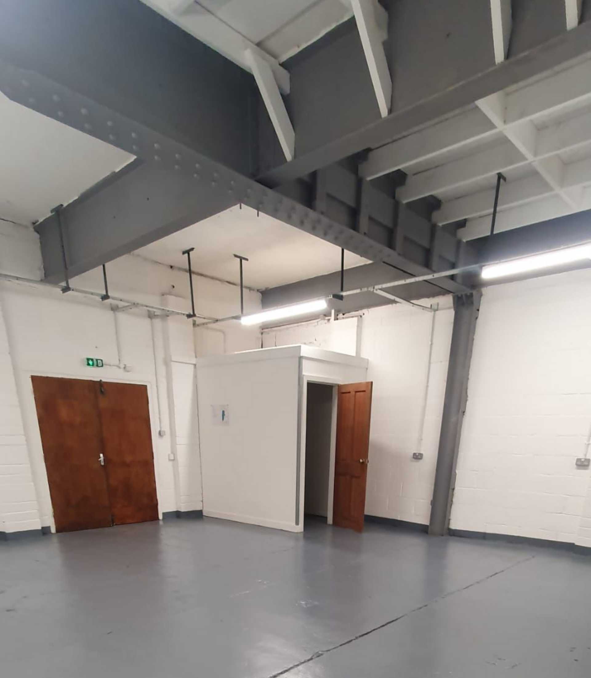 Empty industrial room with gray floor, white walls, exposed beams, and wooden doors.