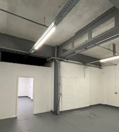 Empty industrial room with white walls, gray floor, exposed beams, and fluorescent ceiling lights