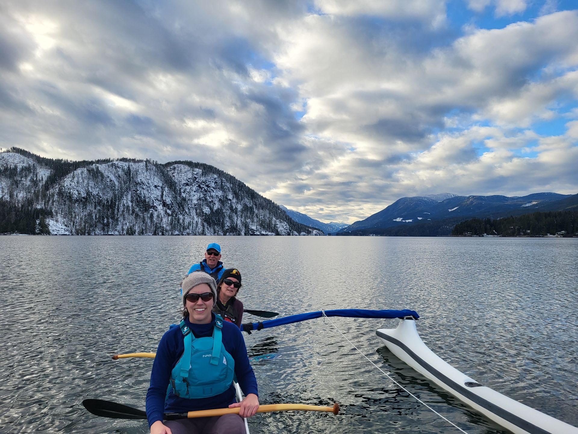 Three people in a canoe on a snowy mountain lake under cloudy skies