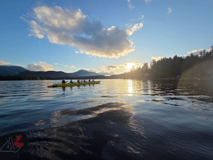 Canoe on a sunlit lake at sunset, with mountains and clouds in the background.