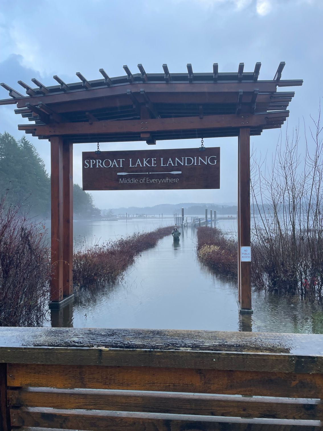 Wooden gate sign at a foggy lake marsh entrance, with a narrow boardwalk leading into the mist.