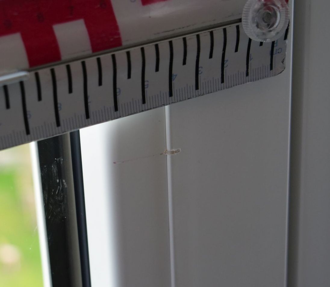 An einer weißen Wand neben einem Fenster hängt ein Lineal.