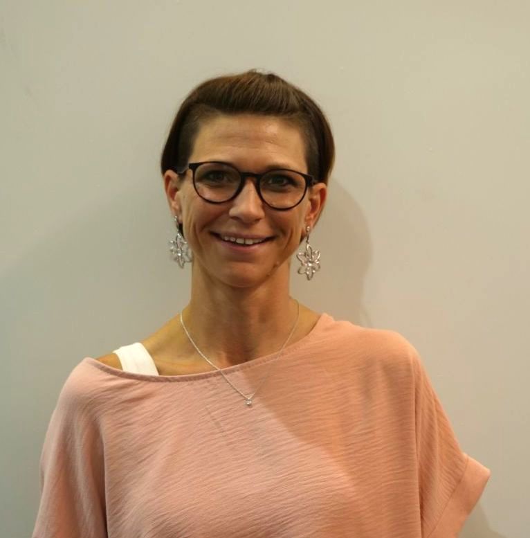 Eine Frau mit Brille und rosa Hemd lächelt in die Kamera