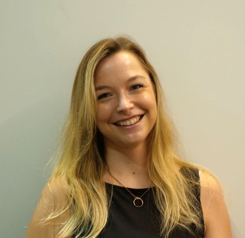 Eine Frau in einem schwarzen Tanktop und einer Halskette lächelt in die Kamera.