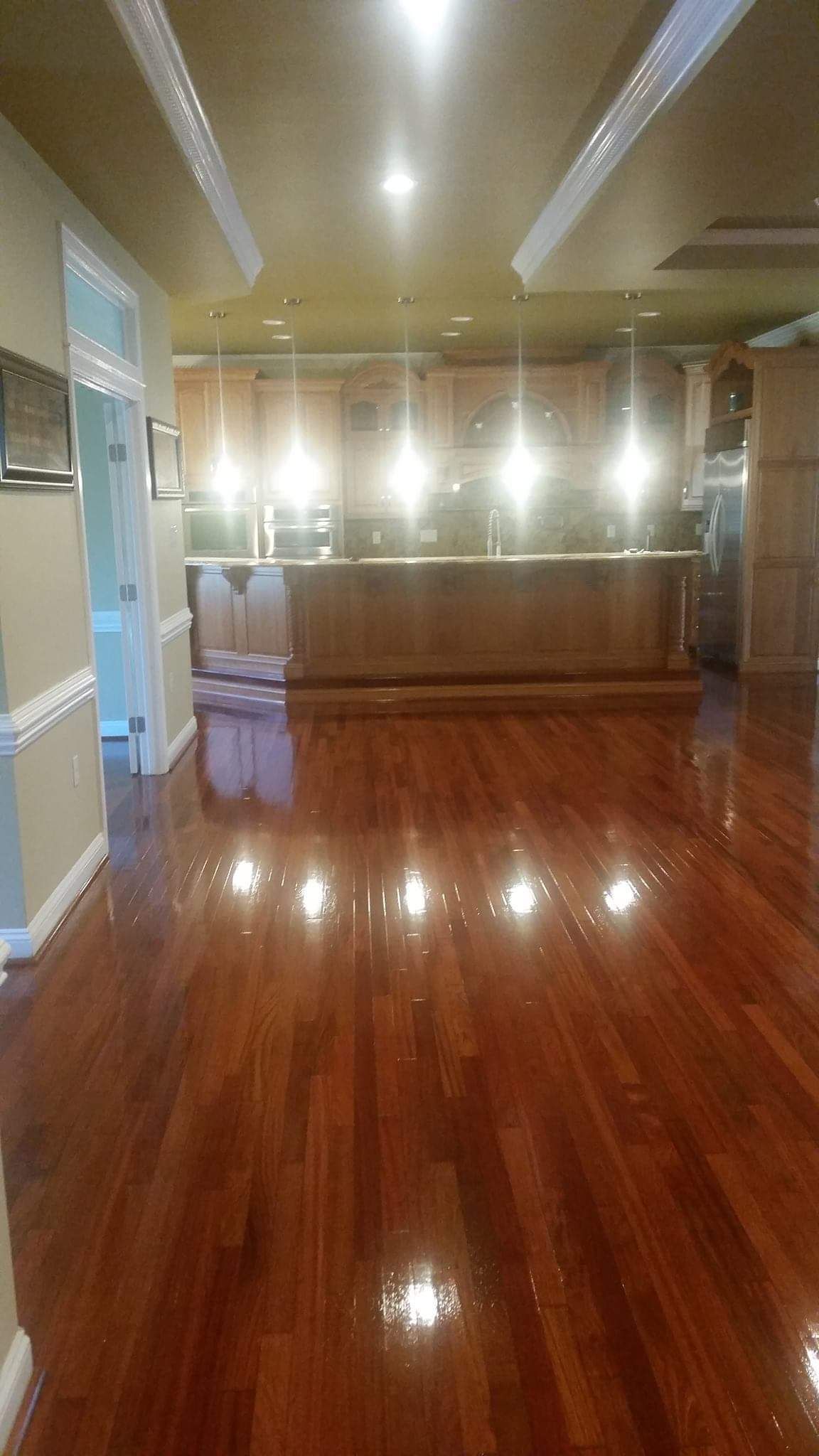 A large empty room with hardwood floors and a kitchen in the background.