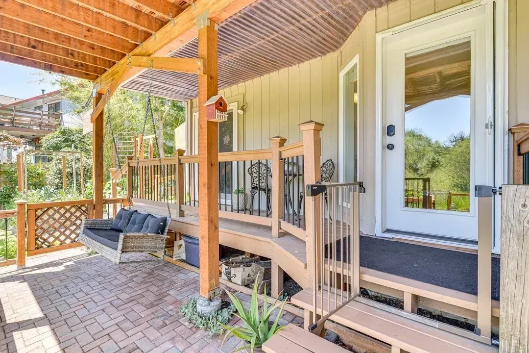 Covered front porch with wooden posts, bench swing, and white door on a beige house