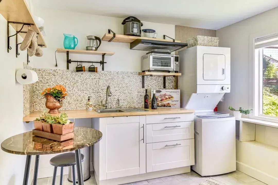 Compact kitchen nook with white cabinets, granite counter, microwave, mini fridge, and window light