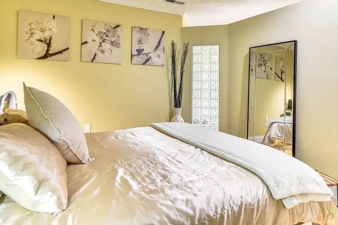 Bright cream bedroom with a made bed, wall art, mirror, and vase of tall branches