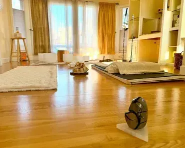 Bright yoga studio with mats, cushions, warm sunlight, and a small fan on the wooden floor