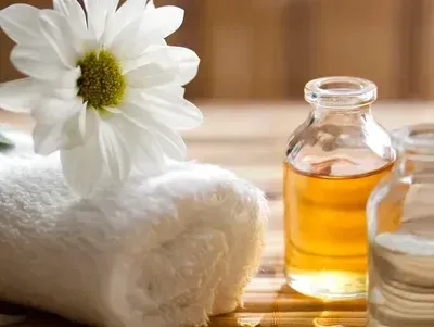 White flower, rolled white towel, and amber oil bottles on a wooden table.