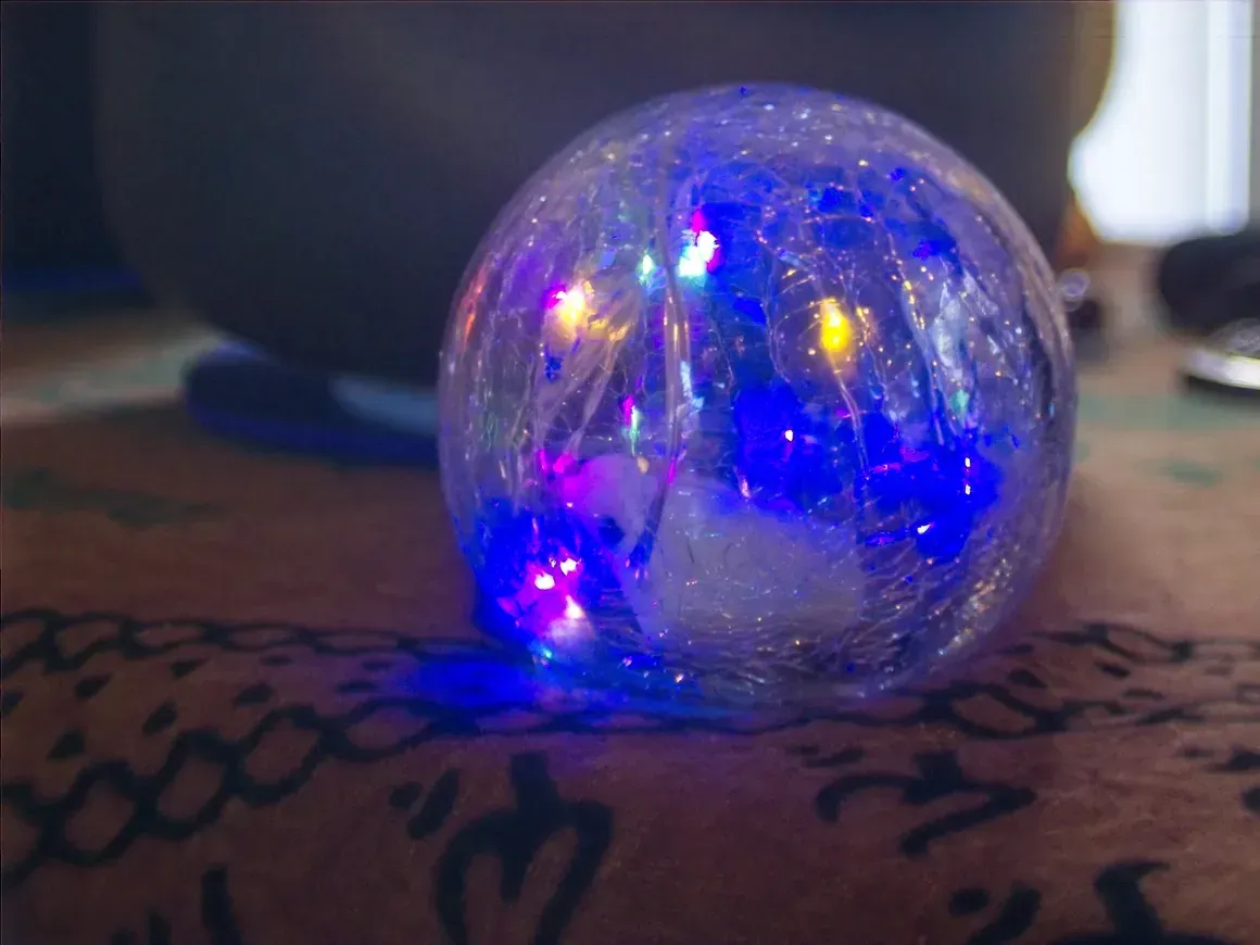 Small clear glass orb with glowing blue and yellow lights on a patterned surface.