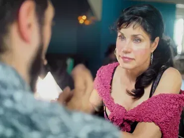 Woman in a pink off-shoulder top listens intently across a table in a dimly lit café.