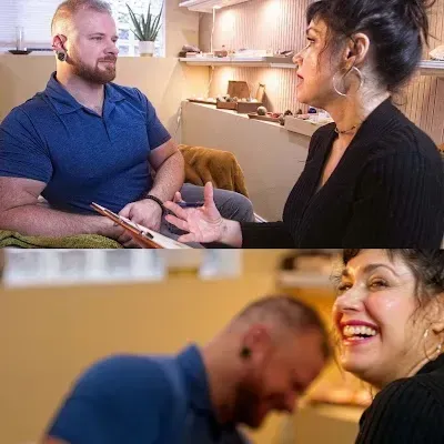 Two people talking in a cozy home, one smiling and gesturing while the other listens attentively.