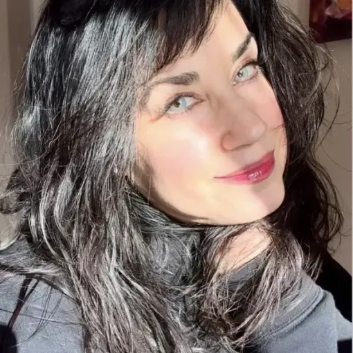 Close-up of a smiling person with dark wavy hair in bright sunlight