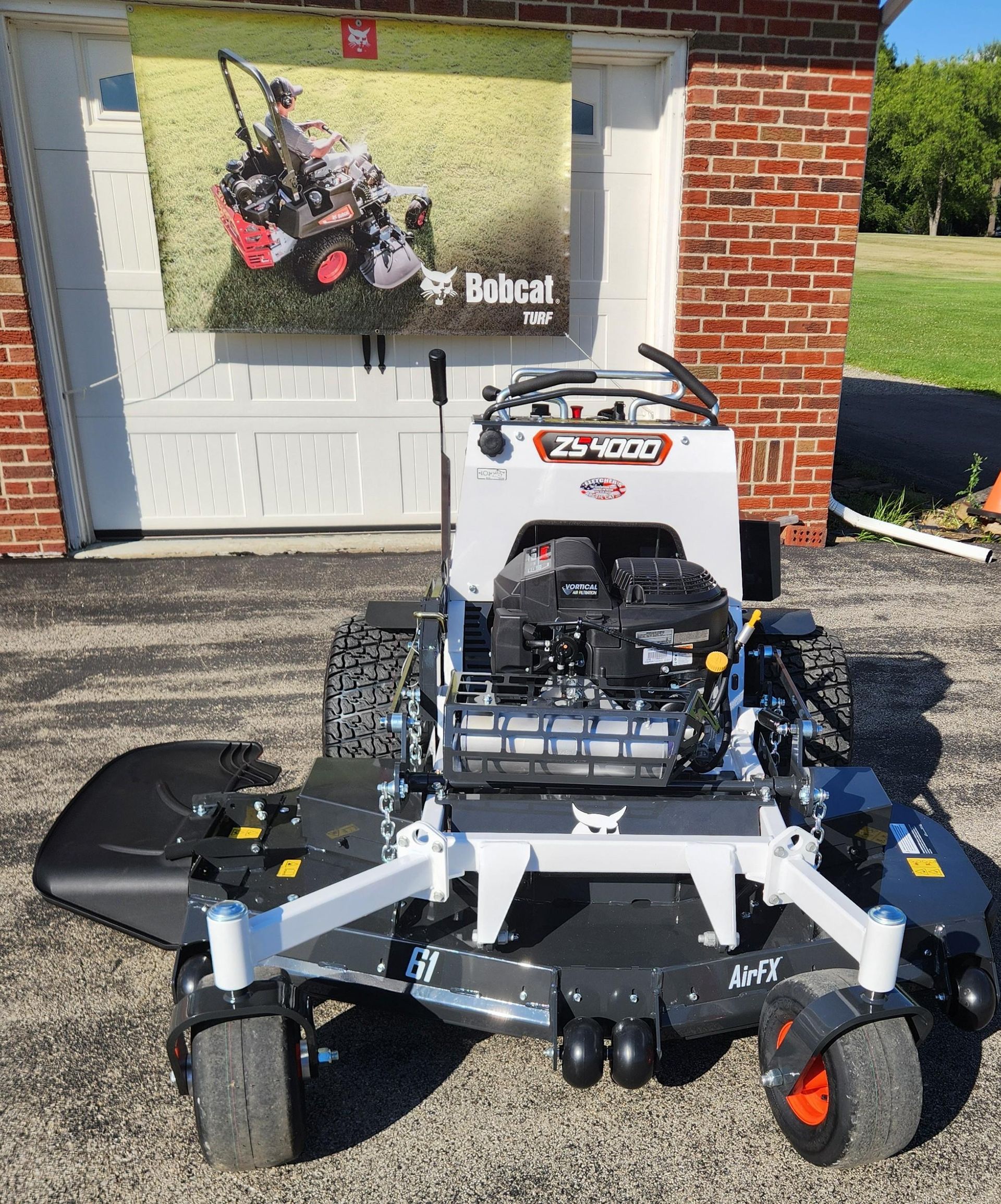 Rear view of a white riding mower on pavement, with black tires and exposed engine components