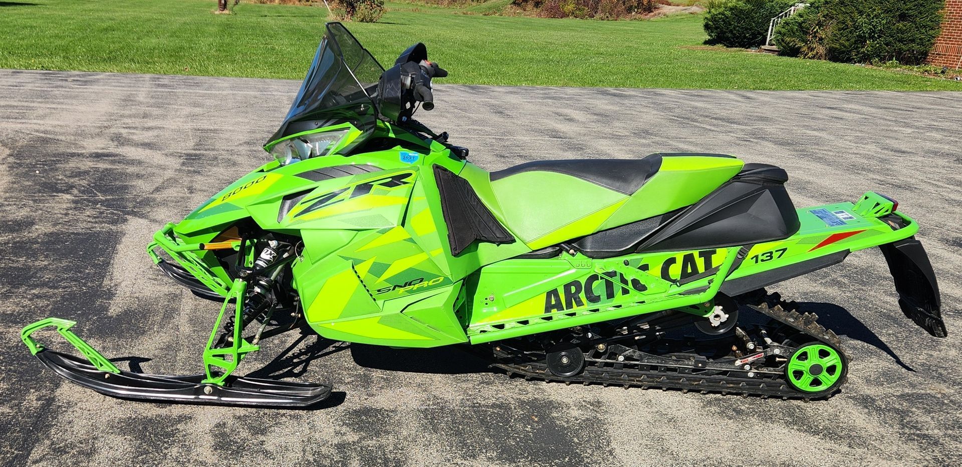 Bright green Arctic Cat snowmobile parked on a gravel path beside grass.