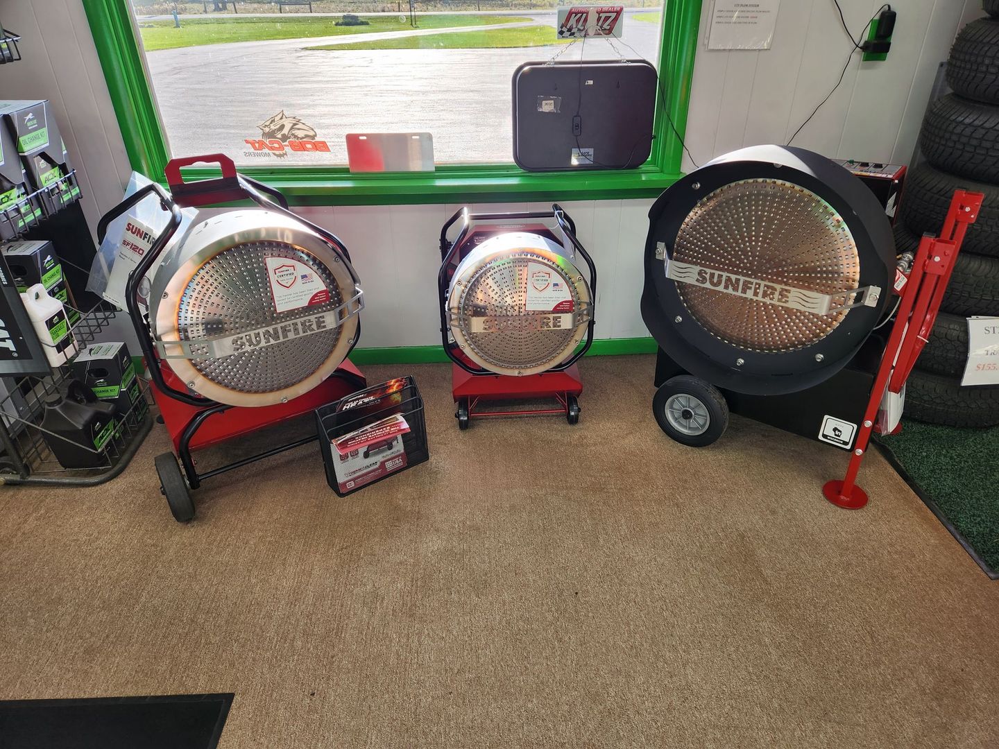 Three industrial fans displayed indoors on a carpeted showroom floor, with a window and green wall behind them