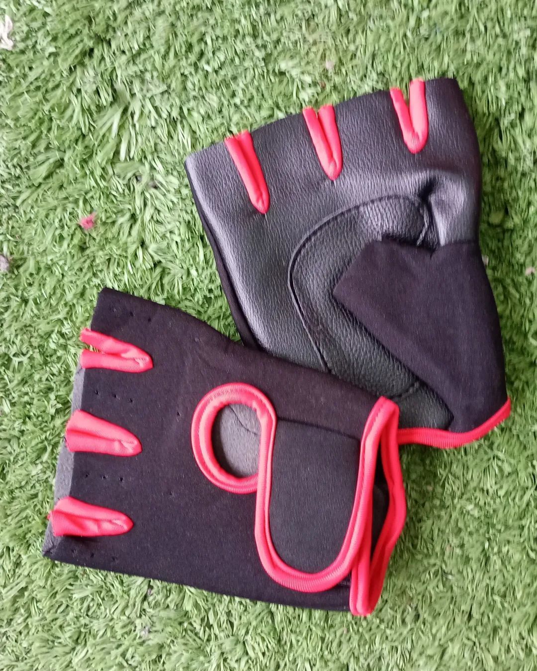 Un par de guantes de gimnasia sin dedos, de color negro y rojo, descansan sobre una superficie verde texturizada.