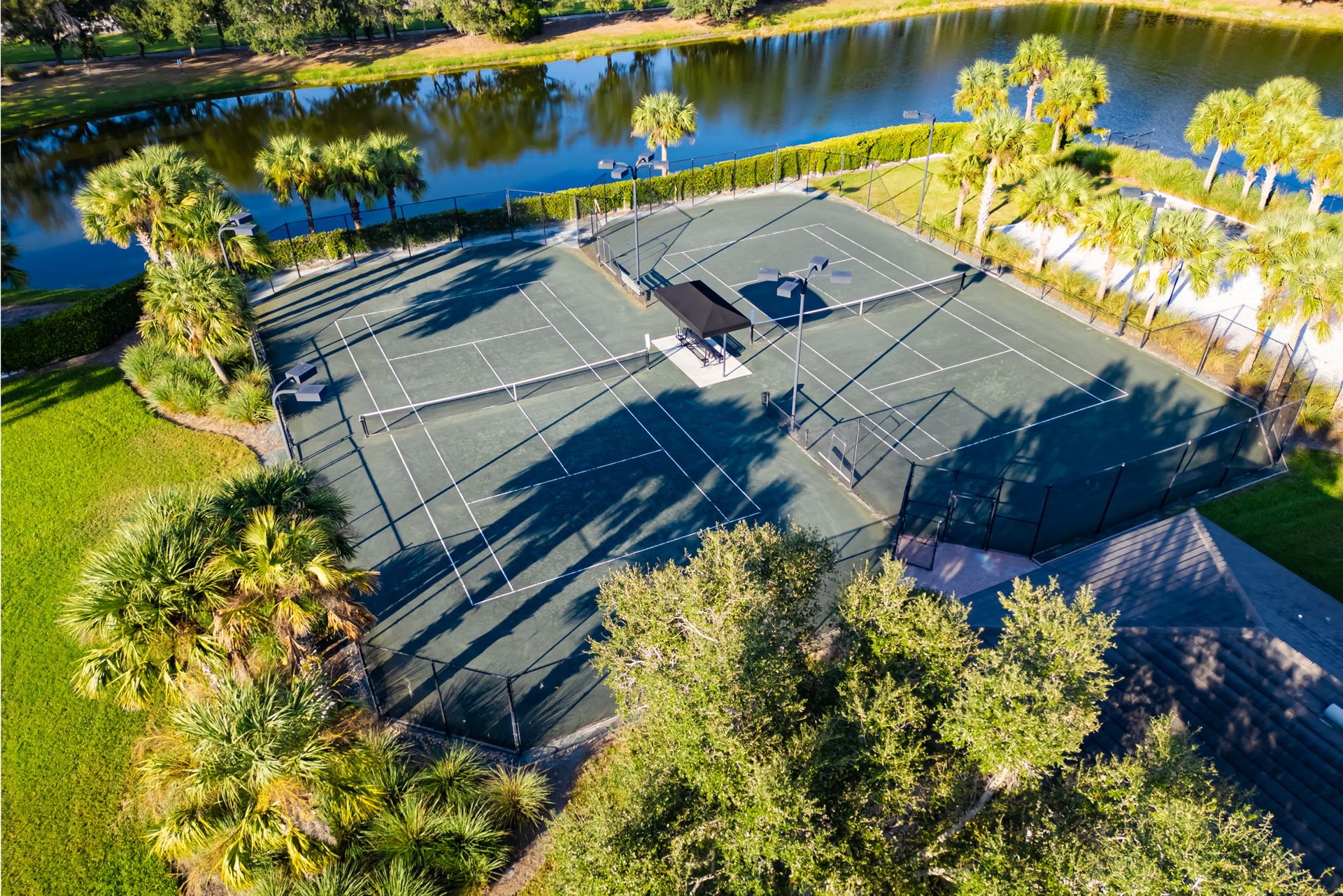 Aerial view of a large gray-roofed building surrounded by trees beside a river.