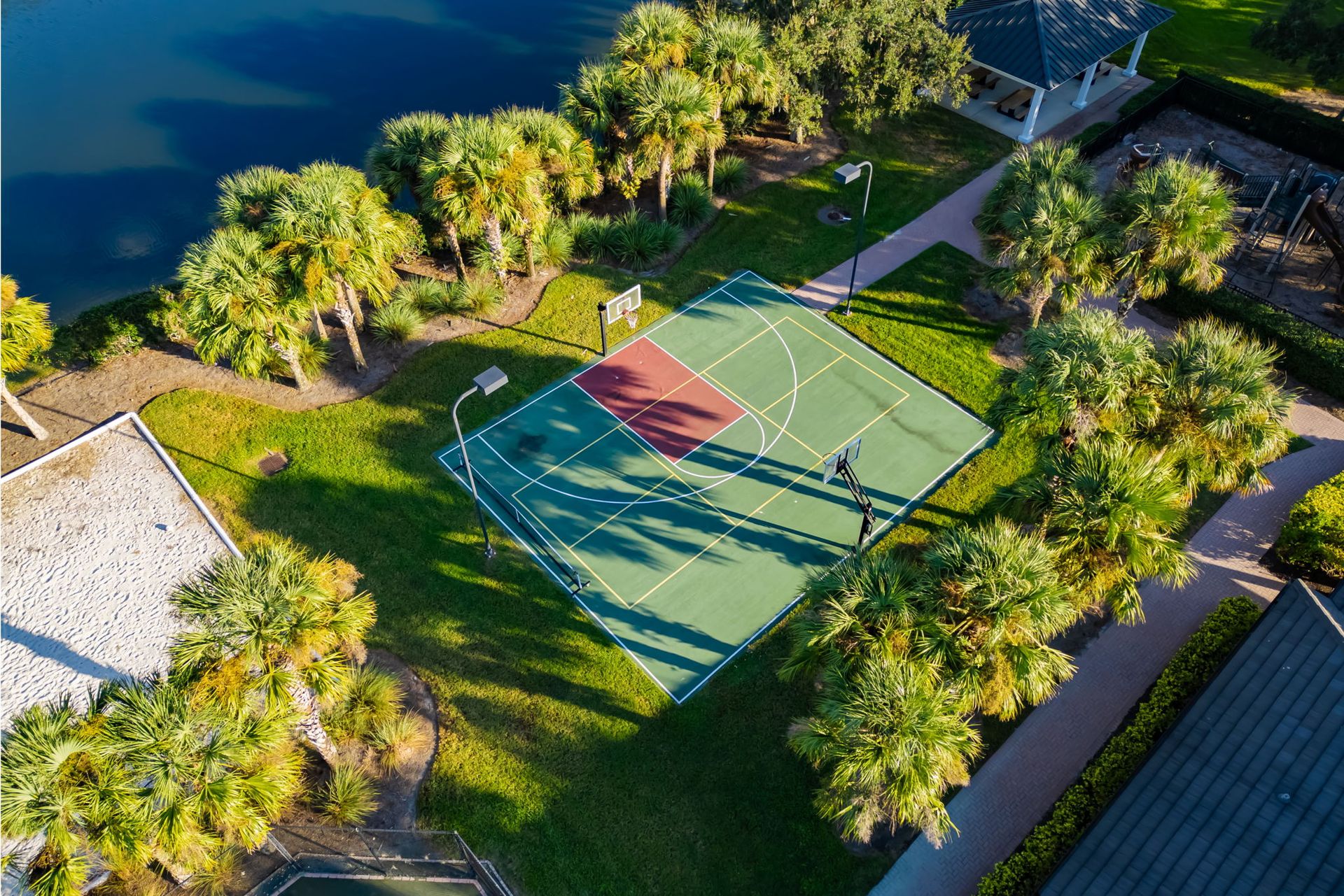 Aerial view of a green tennis court surrounded by trees near water and paths