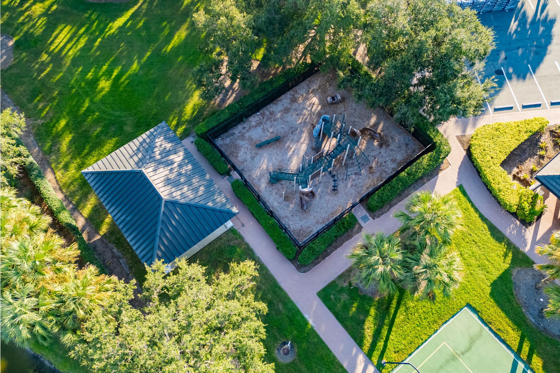 Aerial view of a park with a playground, trees, paths, and a nearby sports court