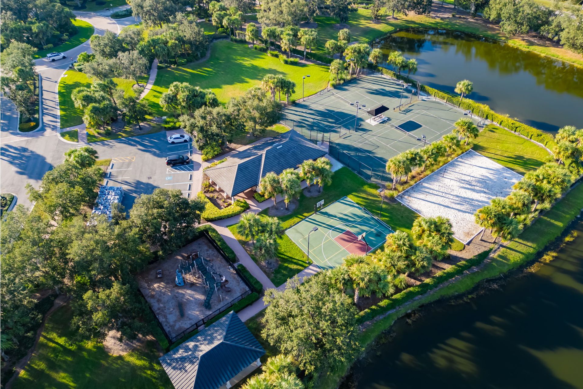 Aerial view of a park with tennis courts, a playground, trees, and a pond