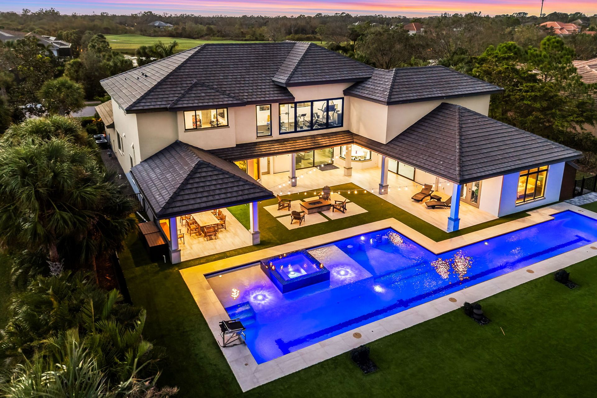 Modern two-story house with lit blue pool and patio at dusk