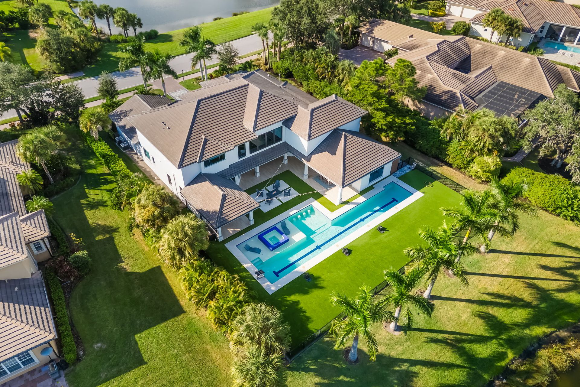 Aerial view of a large modern house with a swimming pool, green lawn, and palm trees.