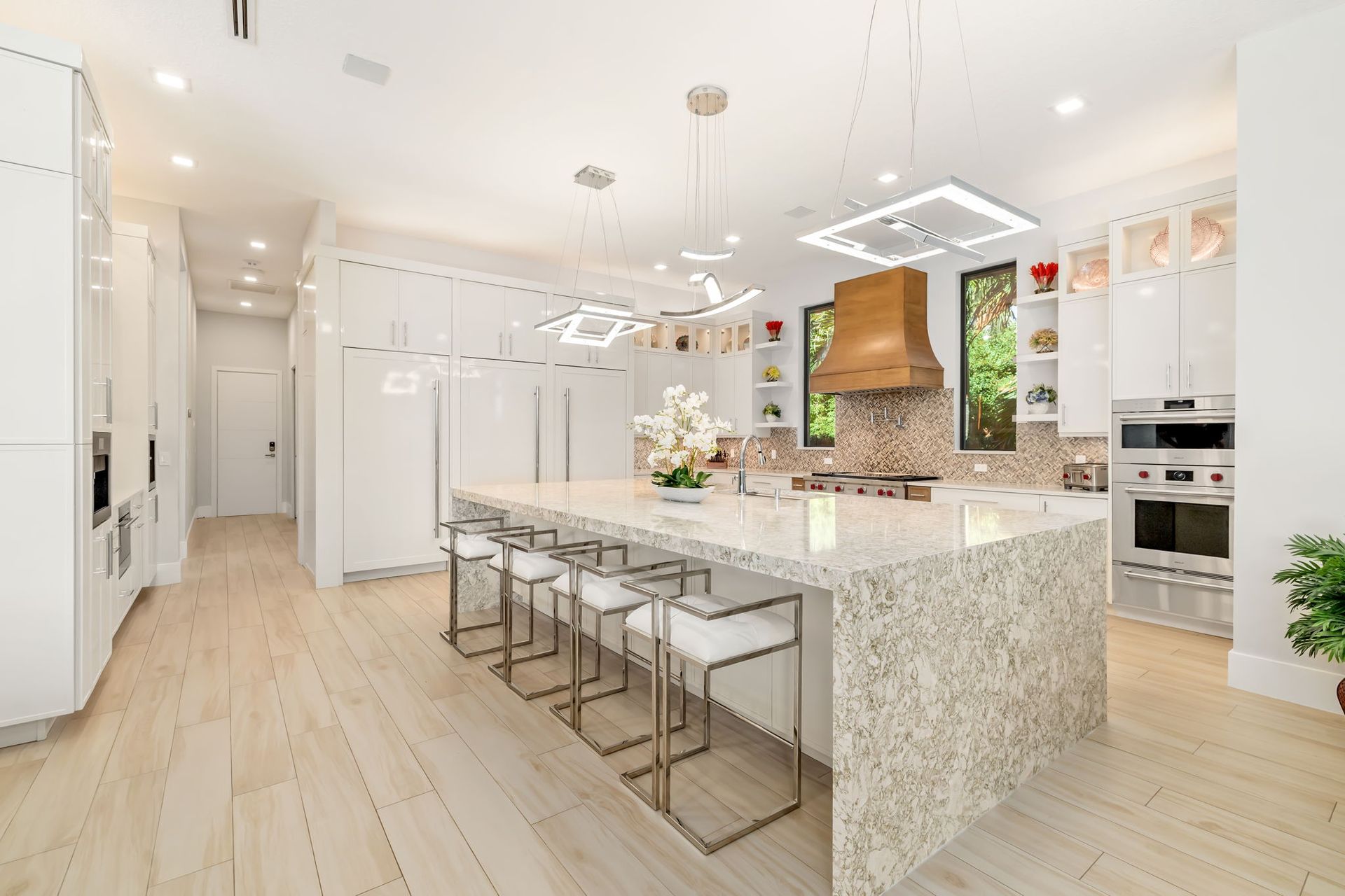 Bright modern white kitchen with large island, bar stools, pendant lights, and pale wood floors