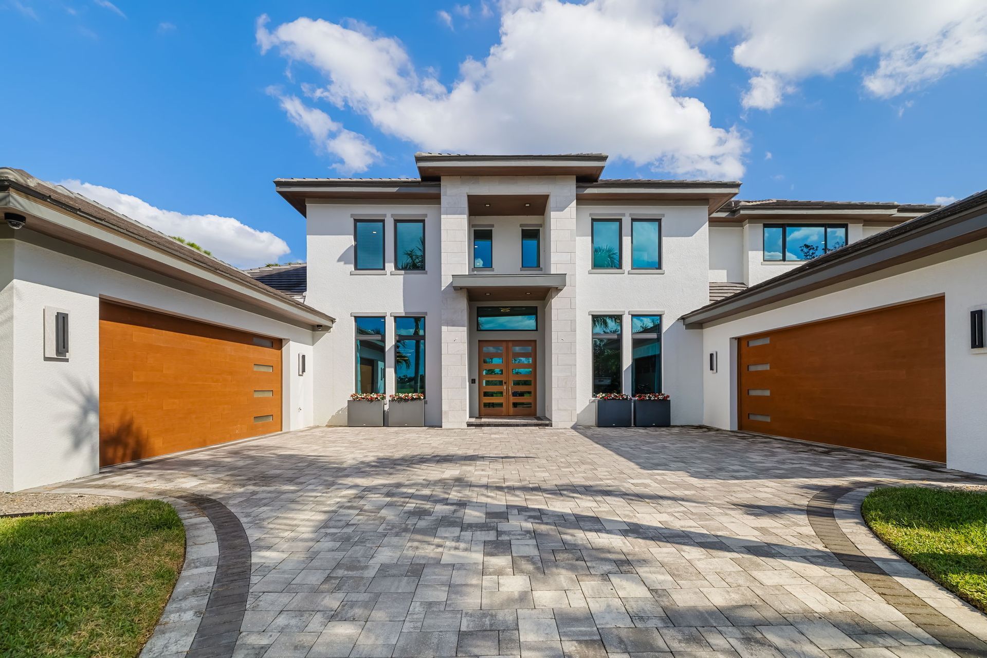 Modern two-story house with a stone driveway, white exterior, and orange garage doors under a blue sky