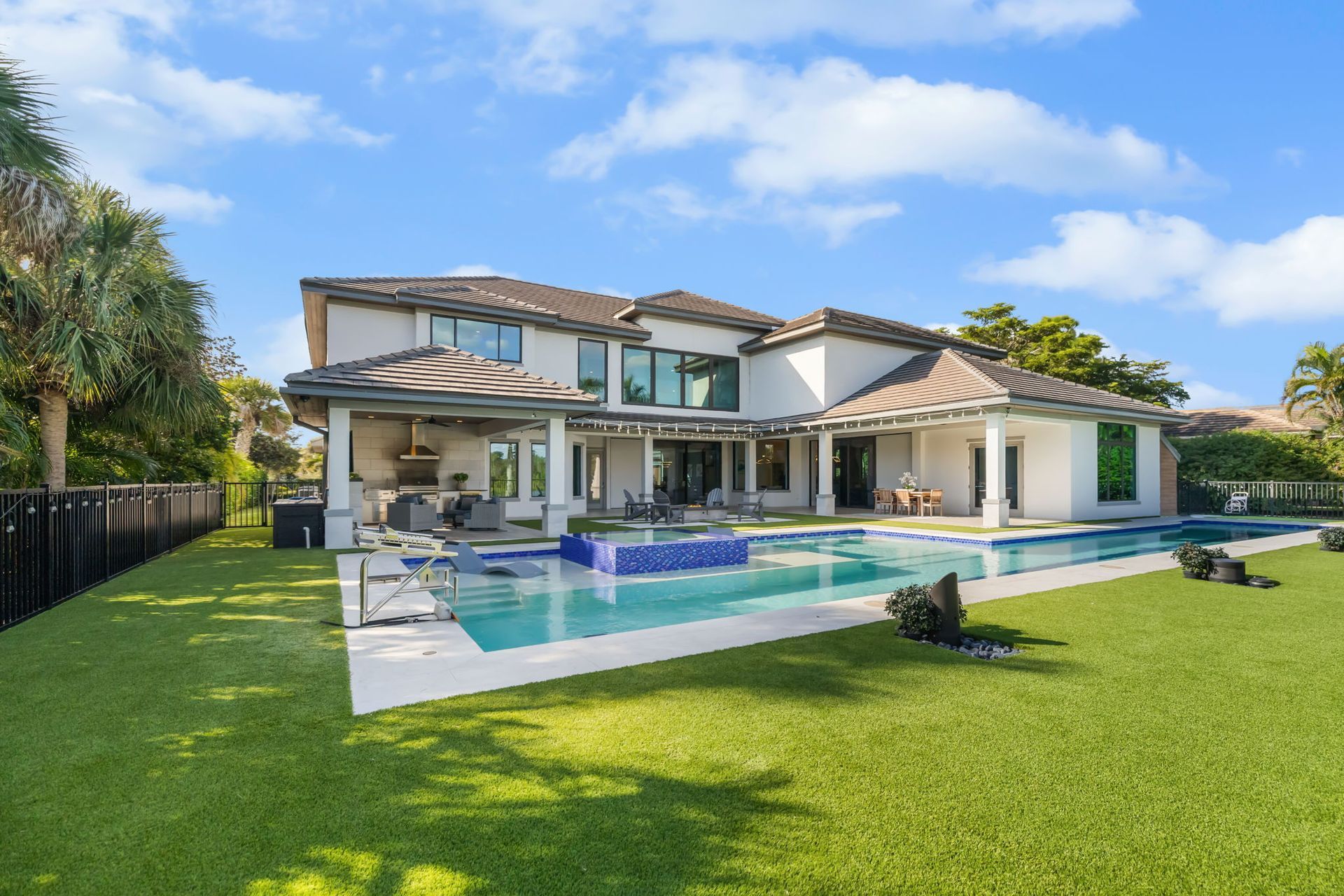 Luxury modern house with a large swimming pool and green lawn under a blue sky