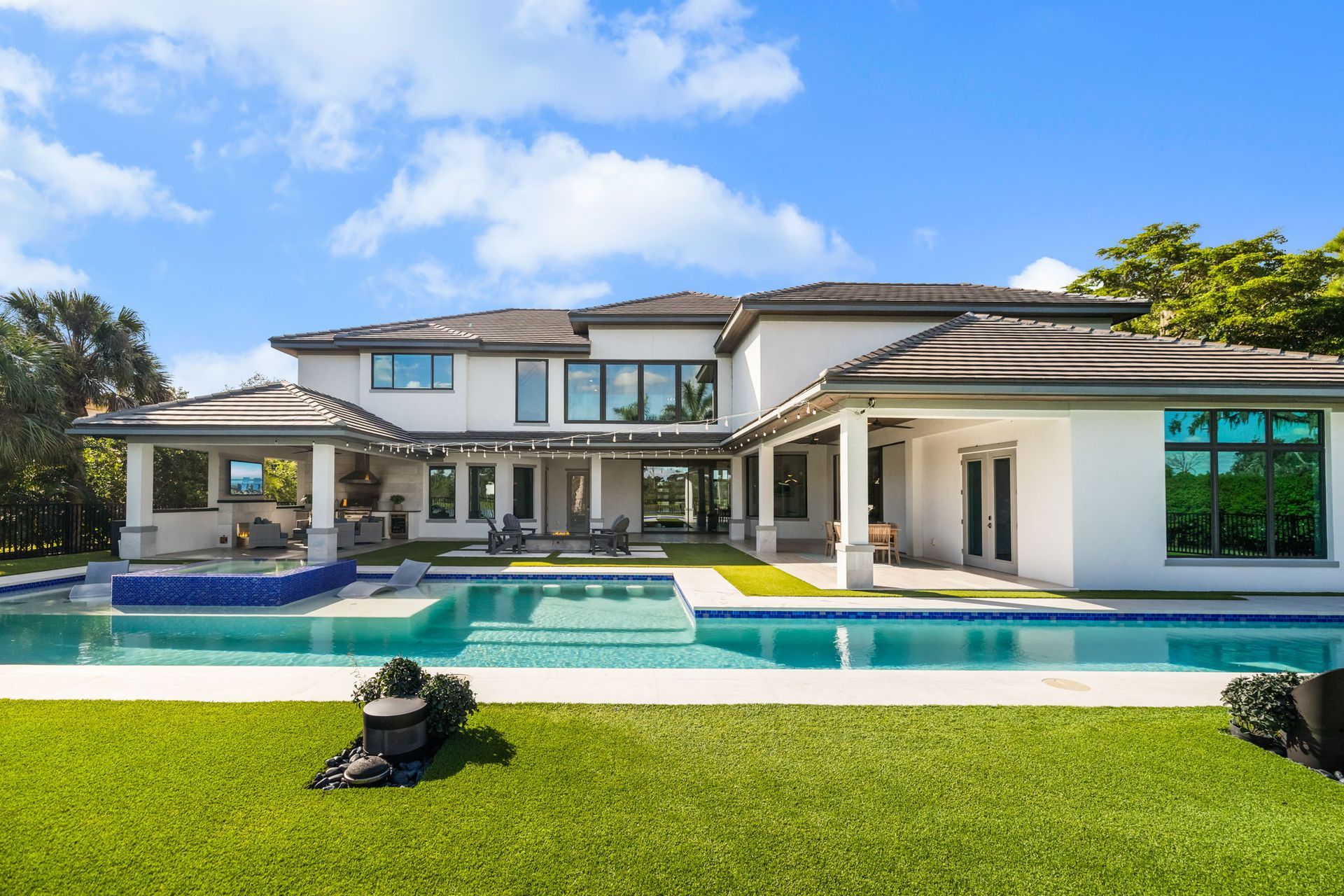 Modern luxury house with a backyard pool, bright green lawn, and blue sky