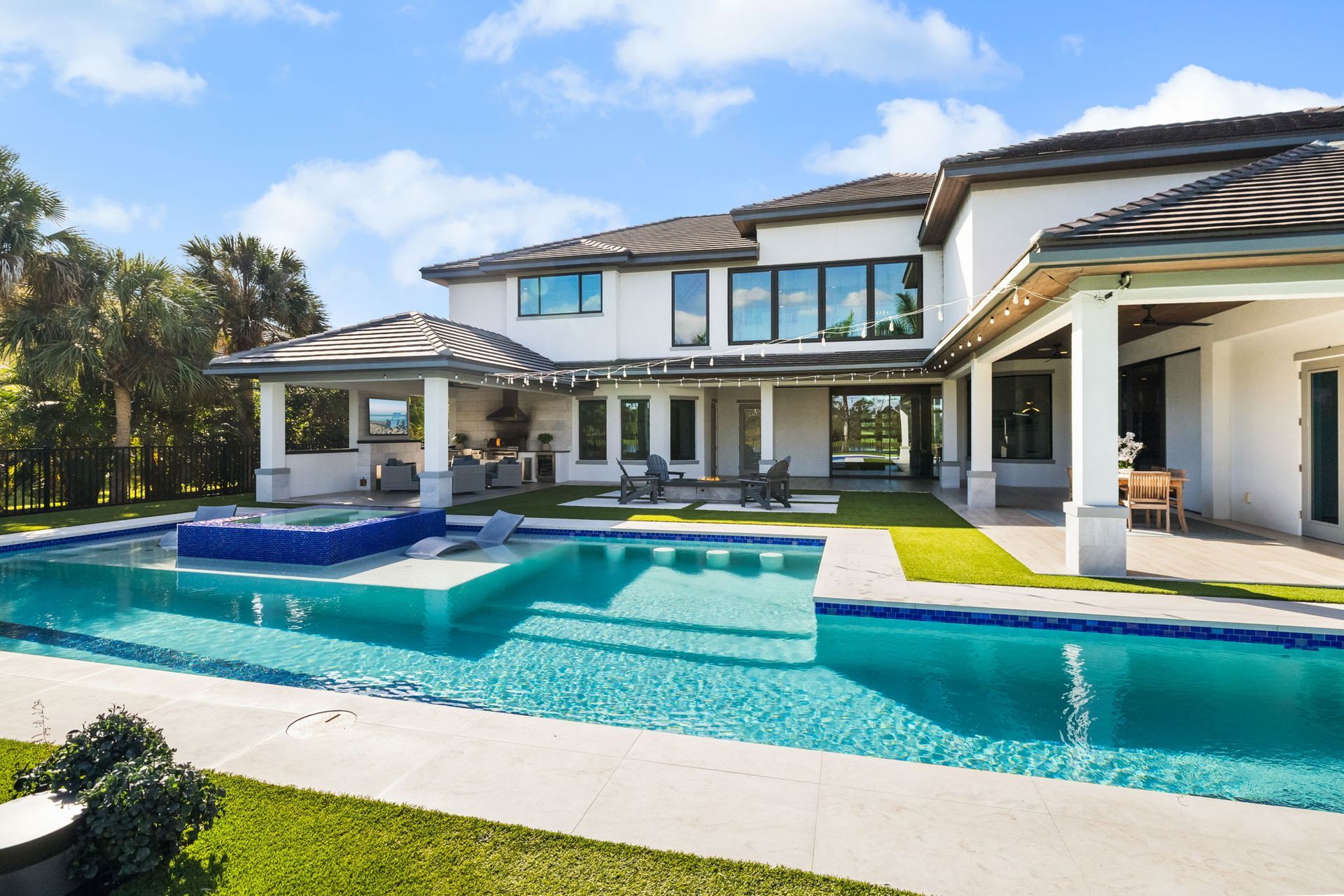 Modern luxury house with a turquoise backyard pool and patio under a bright blue sky