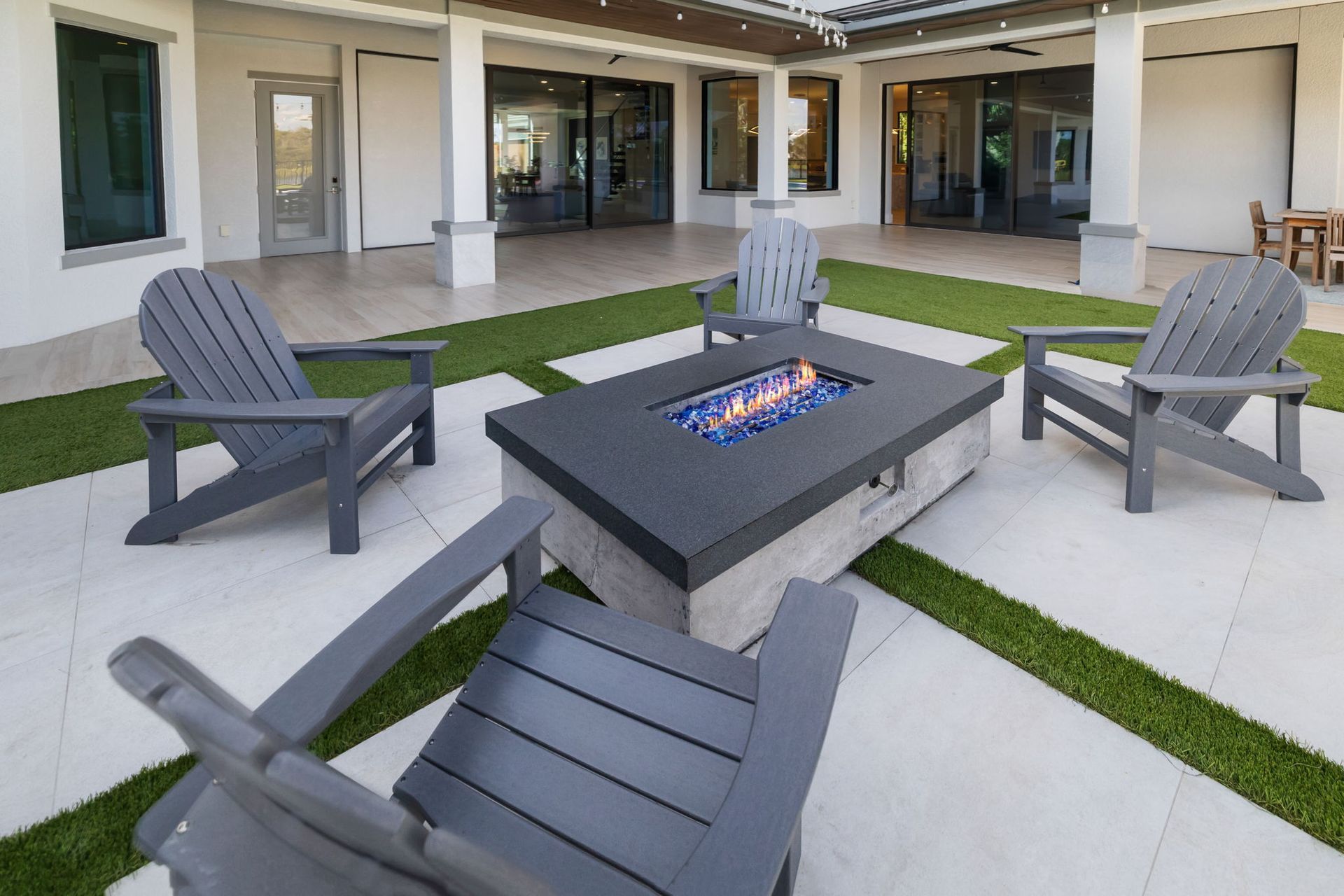 Modern patio seating area with gray chairs around a rectangular fire pit on a tiled courtyard