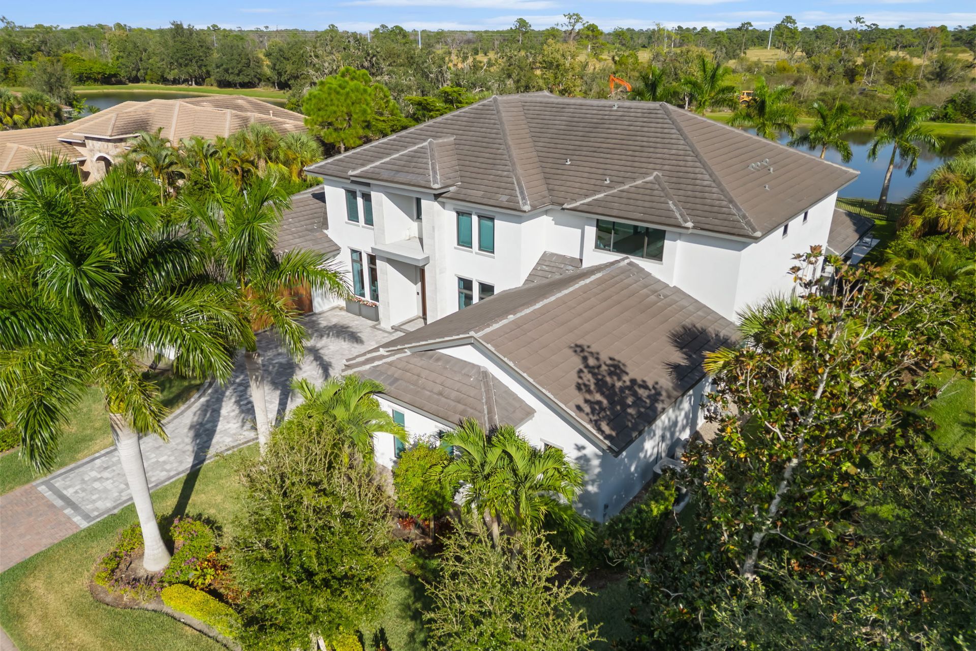 Aerial view of a white two-story house with a gray roof surrounded by lush tropical trees and water.