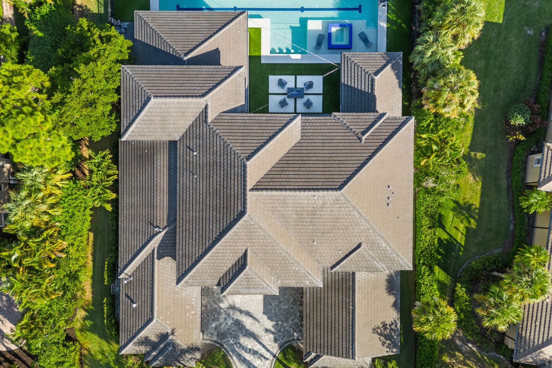Aerial view of a house roof with a backyard pool and surrounding green trees