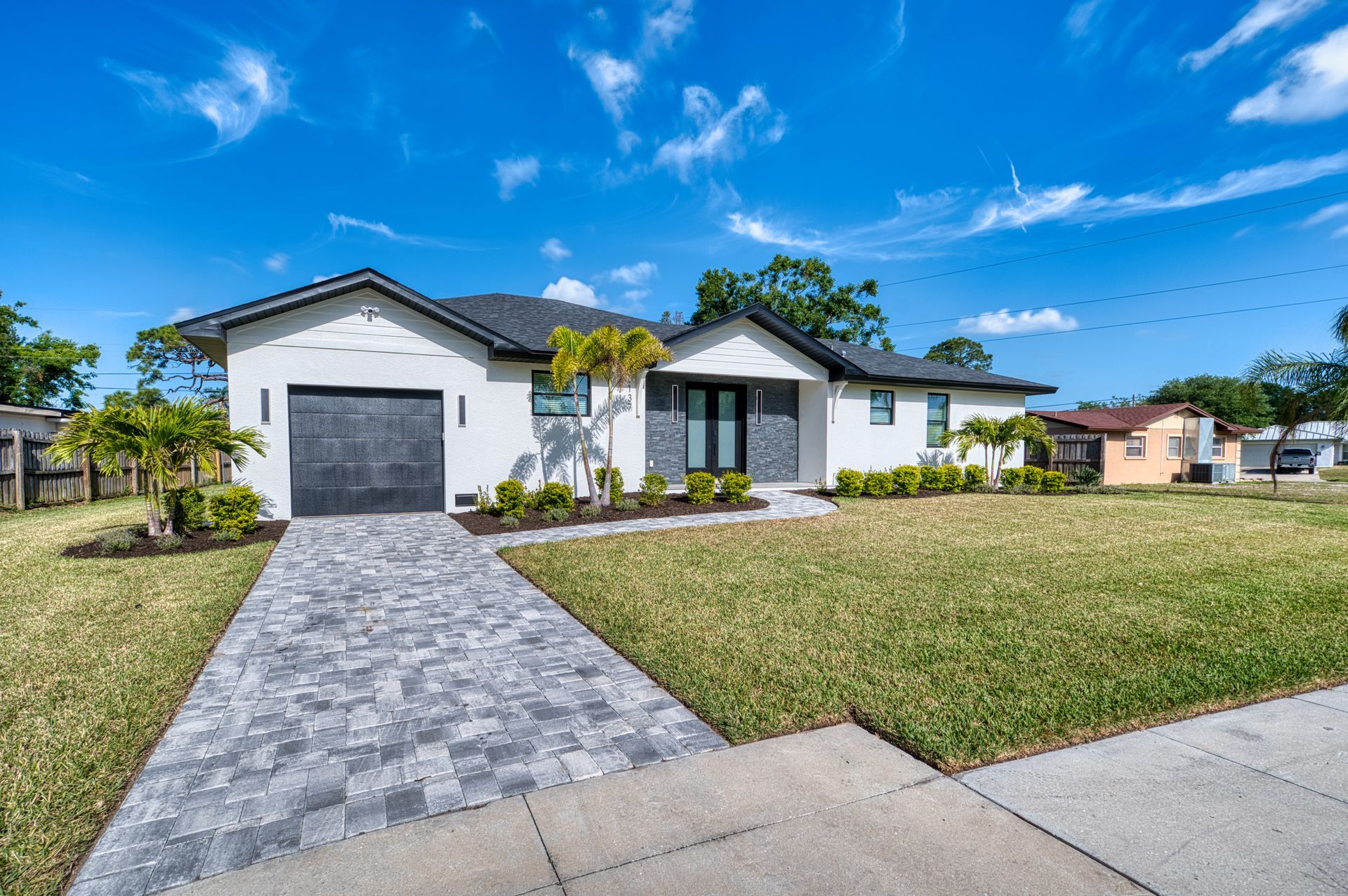 Modern white single-story house with gray stone driveway, green lawn, and blue sky