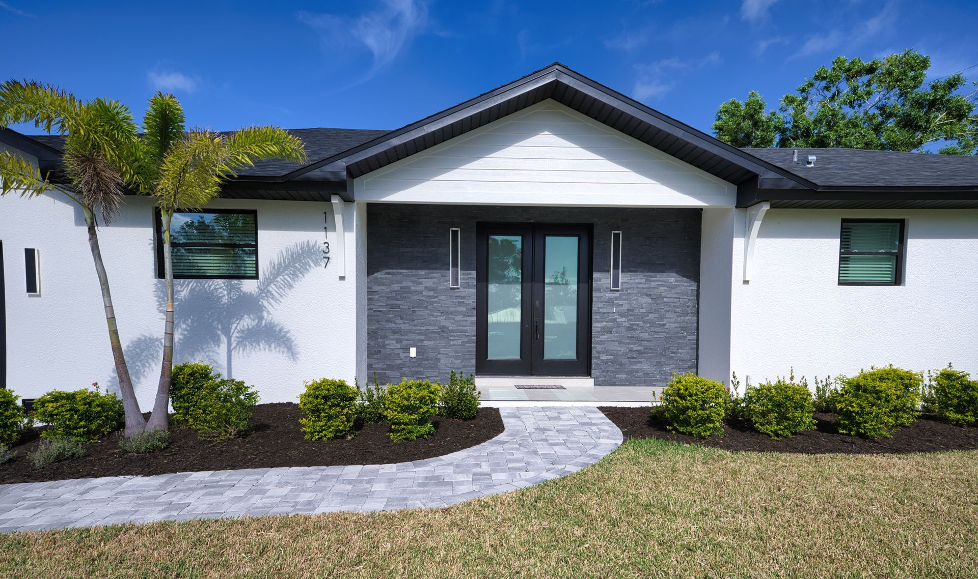 Modern white and gray house exterior with front entrance, stone walkway, and trimmed shrubs