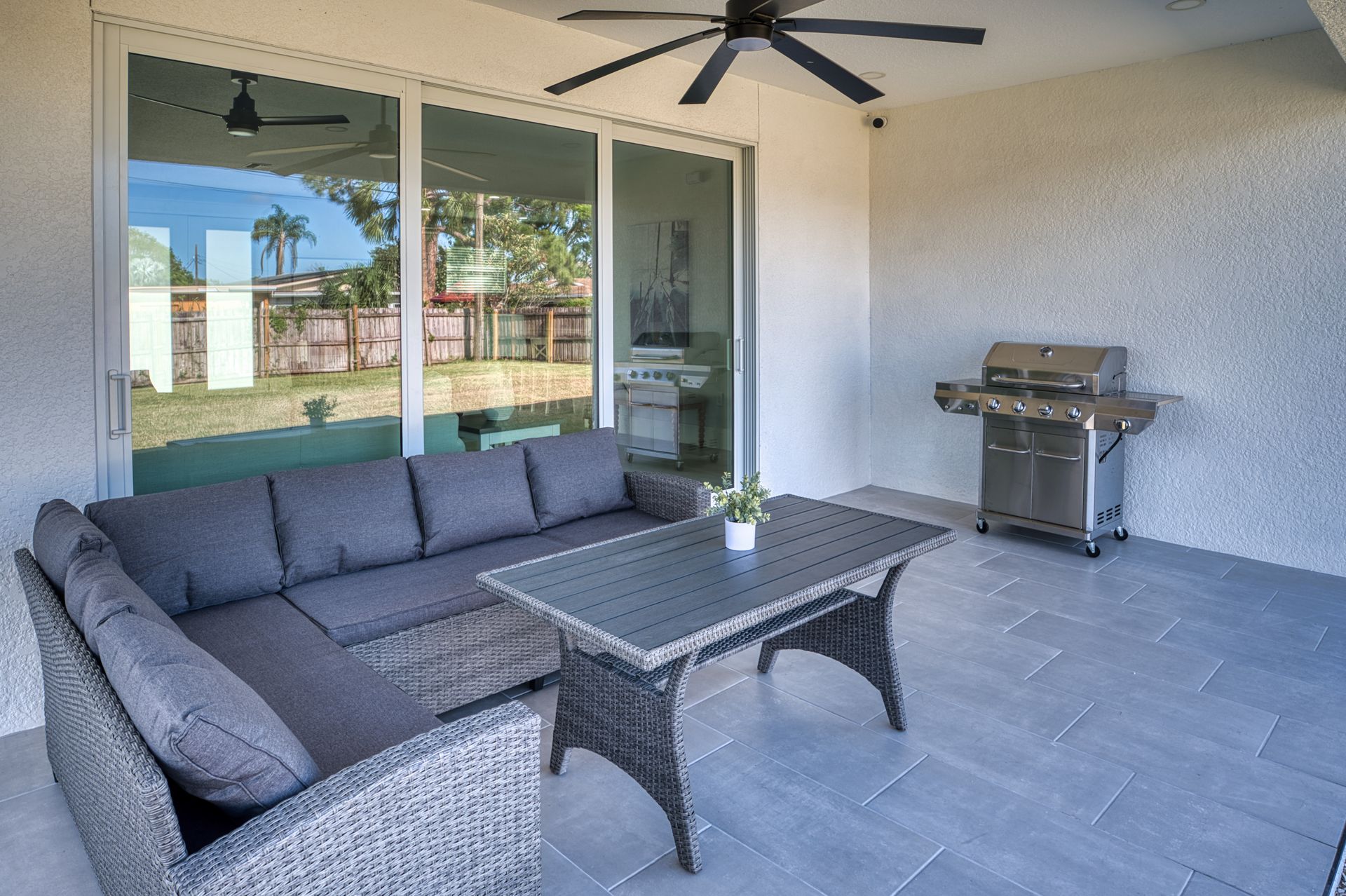 Covered patio with gray sectional, coffee table, ceiling fan, grill, and sliding glass doors