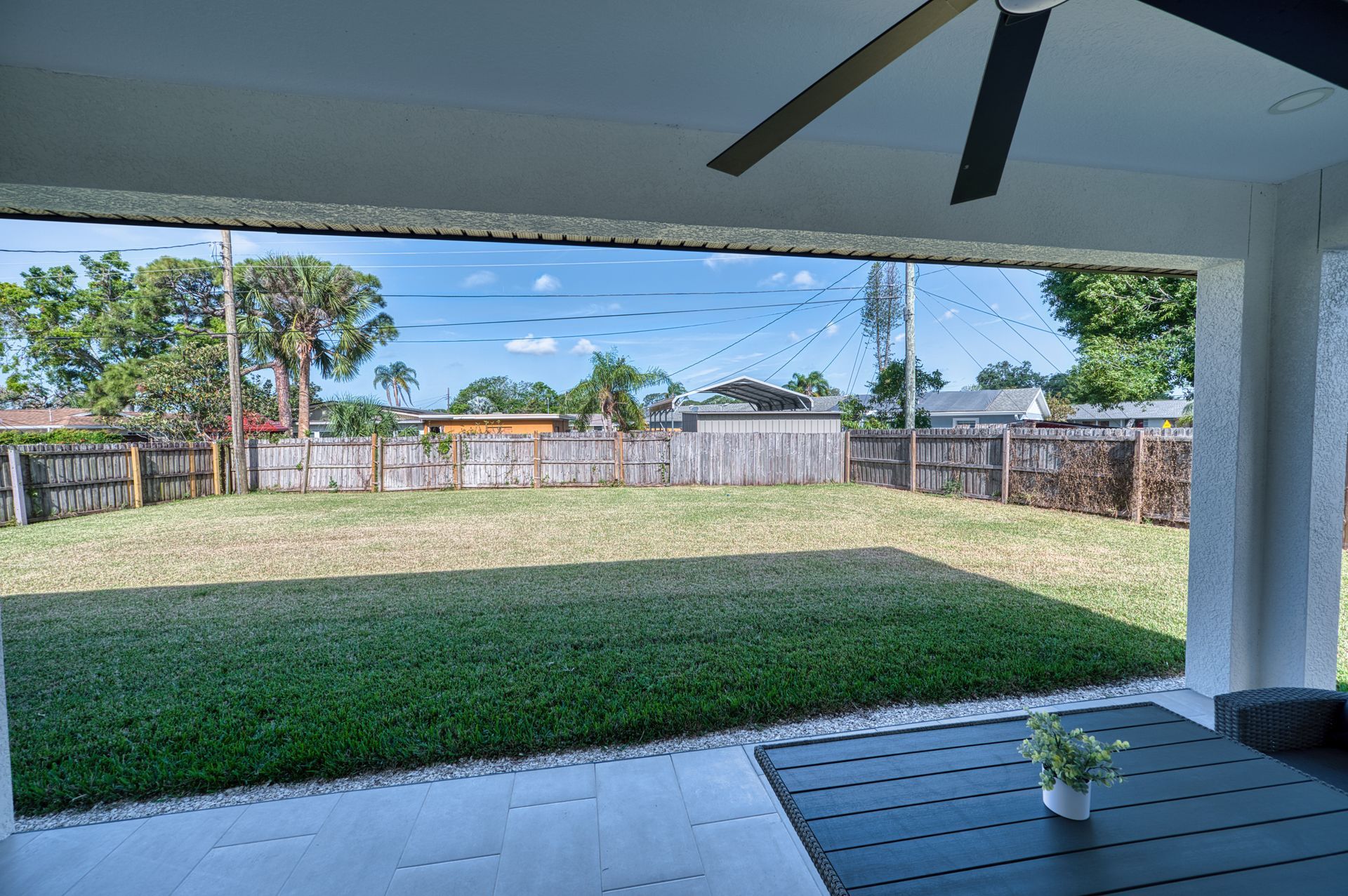 Covered patio overlooking a green backyard and fence, with a table and small potted plant in the foreground