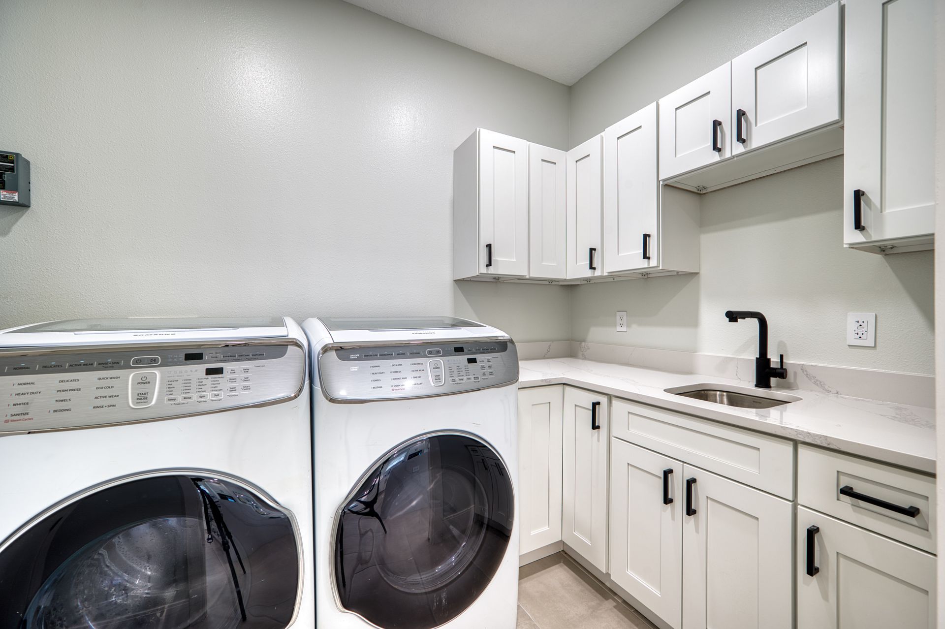 Laundry room with white cabinets, black sink, and washer and dryer against light gray walls.